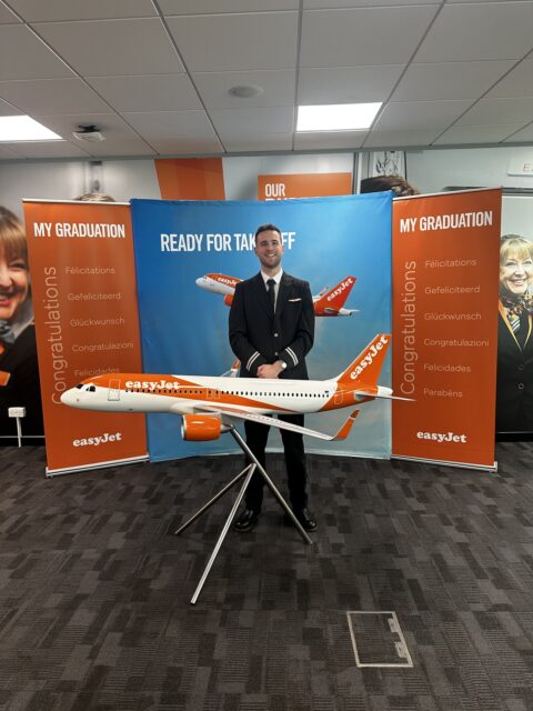 Joshua stands behind a model aeroplane of an EasyJet aircraft.