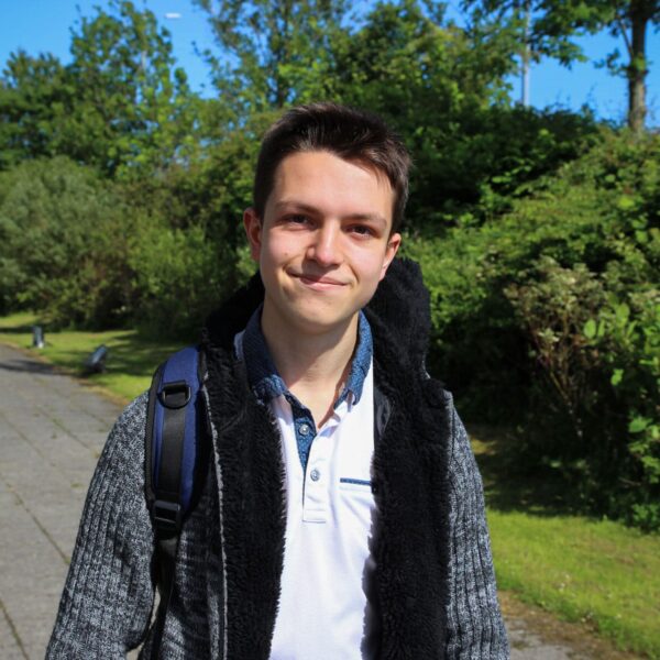 Jacob is stood outside and is wearing a polo shirt with a jacket.