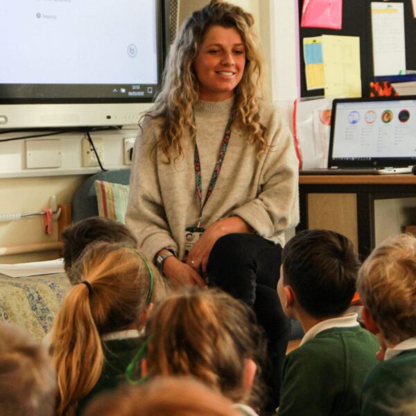 Jess sits in front of small school children who are sat on the floor.