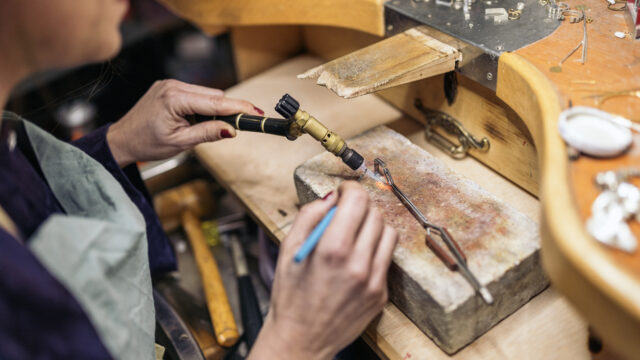 A student doing silversmithing at a work table. They are using a blowtorch.