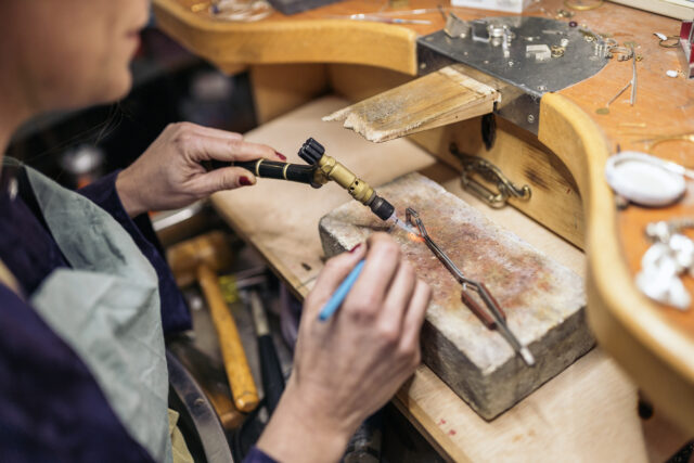 A student doing silversmithing at a work table. They are using a blowtorch.