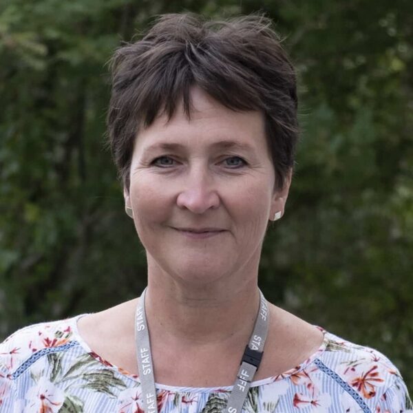A photo of Jo Alker. She is wearing a floral top with her staff lanyard.