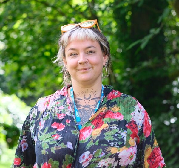Jo is stood outside and wearing a floral shirt.