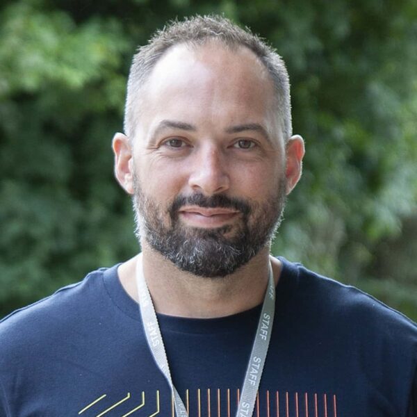 A photo of Joe. He is wearing a dark blue t-shirt and a staff lanyard.
