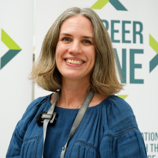 A photo of Katarina, she is wearing a blue top with her staff lanyard and is smiling at the camera.
