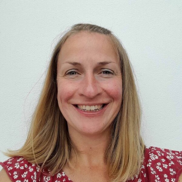 A photo of Kate. She is wearing a red top with white flowers and is smiling against a plain white backdrop.