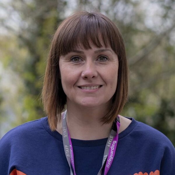 A photo of Kate smiling. She is wearing a jumper with hearts on it and two staff lanyards.