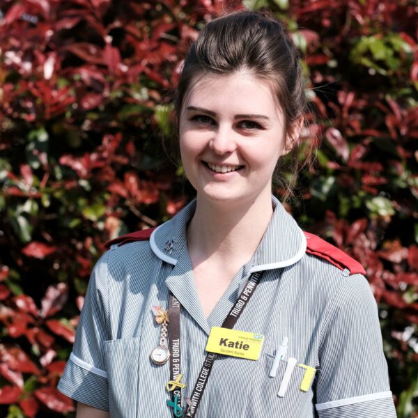 A picture of Katie in her nurse's uniform. She is wearing a lanyard, has her hair tied up and has a stopwatch and pens in her pockets.