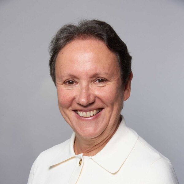 A photo of Kay Penney, she is wearing a white shirt and is against a grey backdrop.