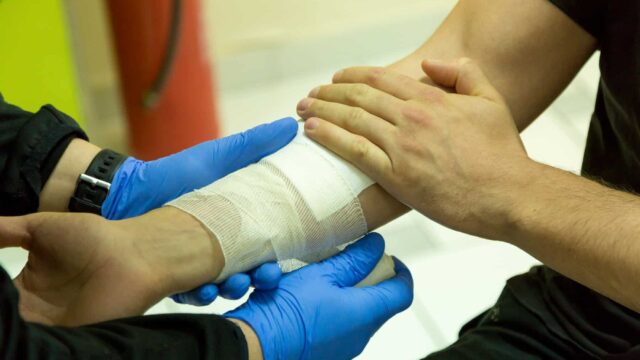 Close up of gloved hands putting a bandage on an arm.