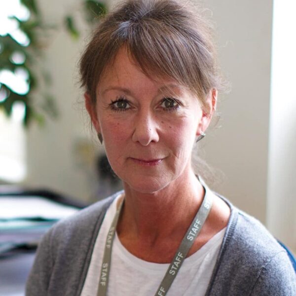 A photo of Laura, she is wearing a white t-shirt, a grey cardigan and her staff lanyard.