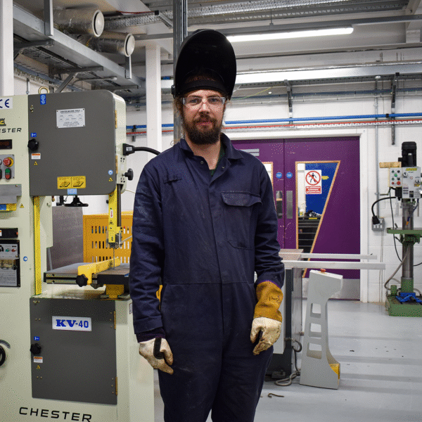 A student is wearing overalls, gloves and a welding mask.