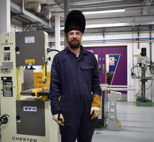 A student is wearing overalls, gloves and a welding mask.