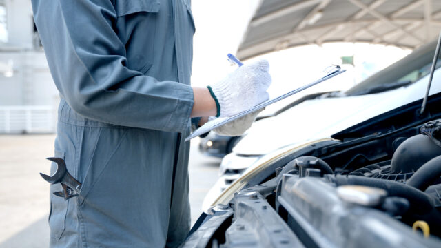 Mechanic checking on a car engine and taking notes.