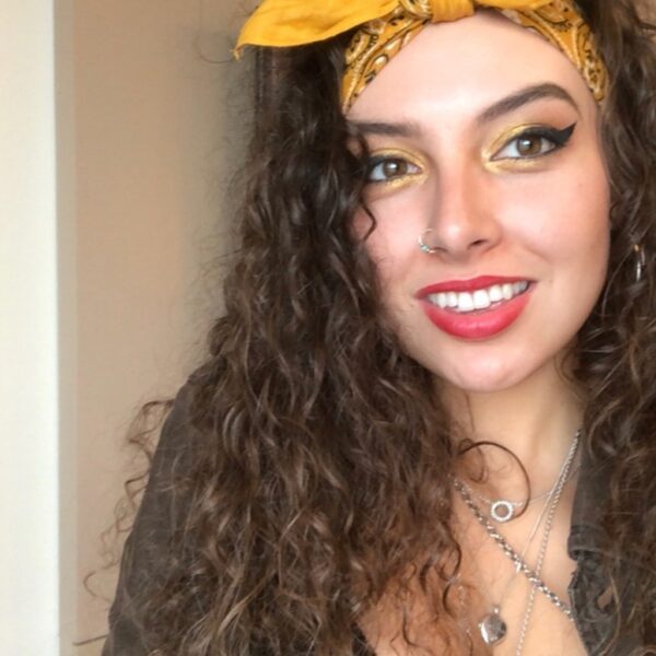 Miranda has long curly hair with a yellow bandana and bright make-up.