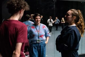 A tutor standing with students in a drama studio with large mirrors.