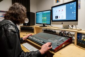 A music student sat at a table with music technology equipment in front of him and a computer.