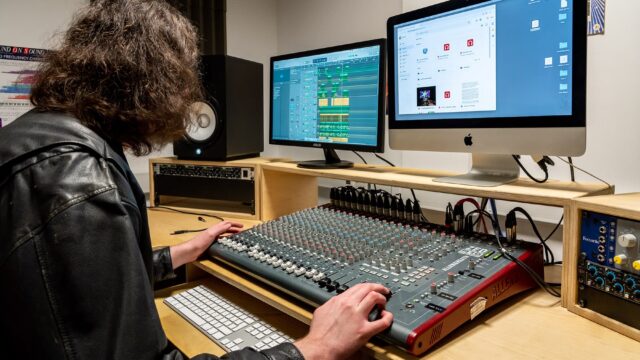A music student sat at a table with music technology equipment in front of him and a computer.