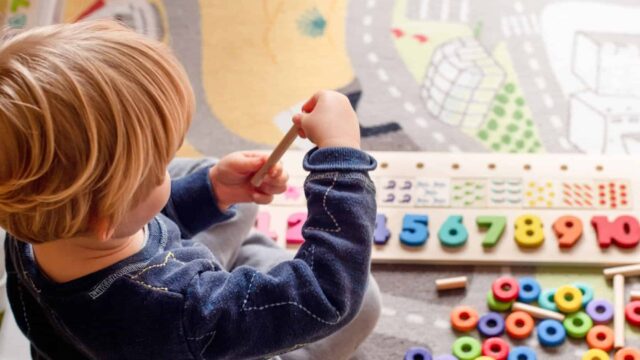A child sits on the floor and plays with brightly coloured wooden toys.