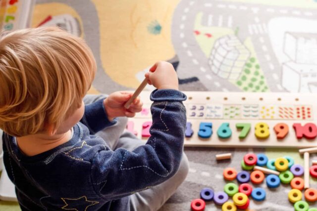 A child sits on the floor and plays with brightly coloured wooden toys.