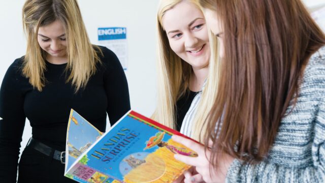 Three students look through a childern's book together.