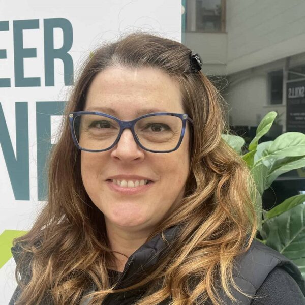 A photo of Niki, she is wearing a black jacket and glasses and is smiling at the camera.