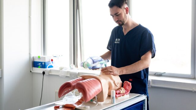 A medical student uses a breathing apparatus on a dummy.