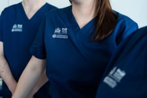 A close up of navy scrubs with the college logos and University of Greenwich logo embroidered on them.