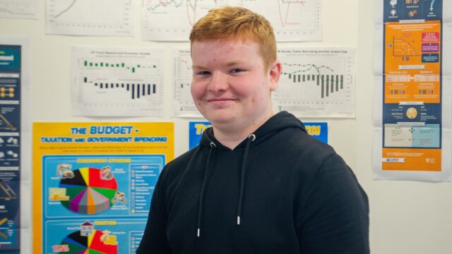 A smiling student who has posters of pie charts and graphs behind them.