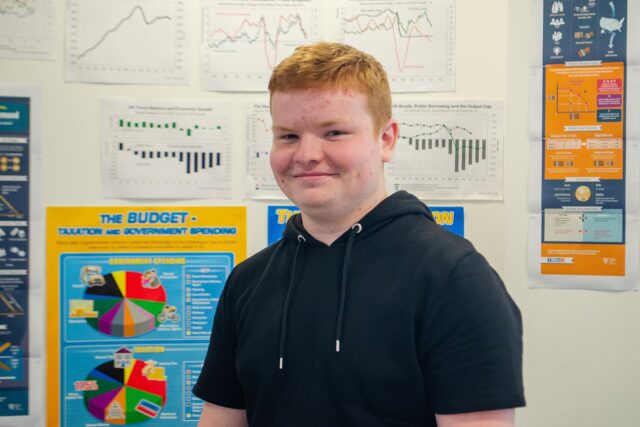 A smiling student who has posters of pie charts and graphs behind them.