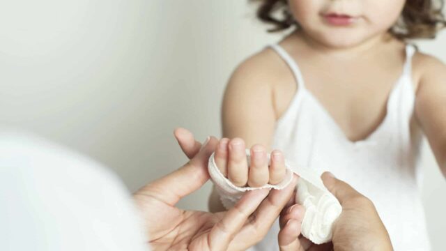 An adult puts a bandage around a child's hand.
