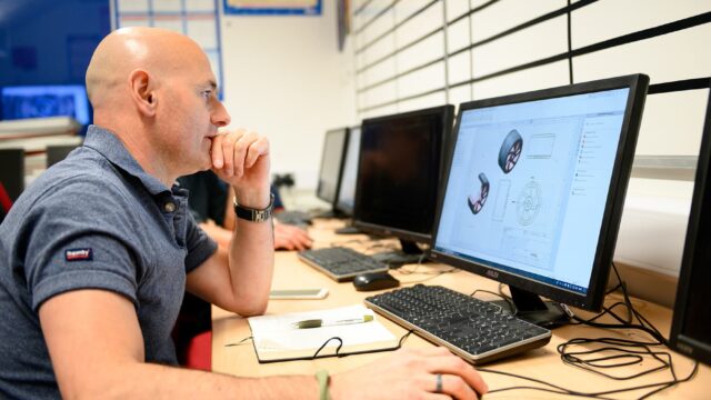 A man sat with a computer in front of him that shows a diagram of a wheel.