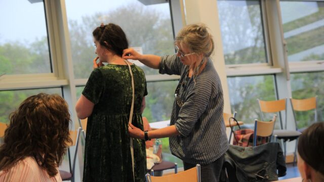 A tutor takes a measurement down a model's back.