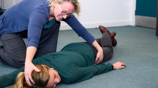 A person practices moving another person into the recovery position.