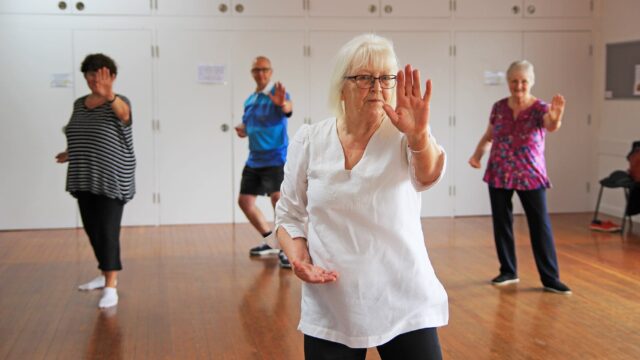 Four people stand in a dance hall doing tai-chai.