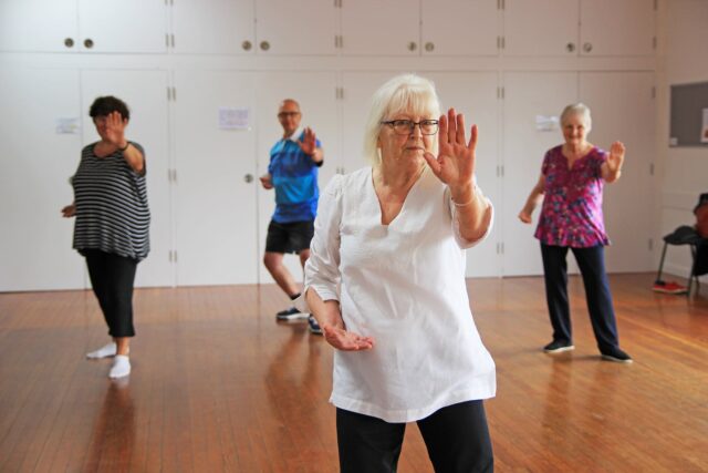 Four people stand in a dance hall doing tai-chai.