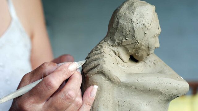 A close-up of a person carving a sculpture from clay.