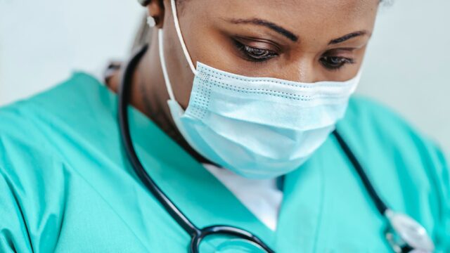 A close-up of a nurse wearing a surgical mask and scrubs with a stethoscope around their neck.