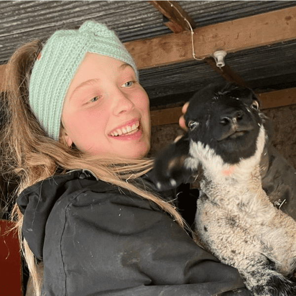 Phoebe holds a lamb in a barn.