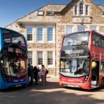 Two buses are parked in front of a college building and students are hopping onboard.