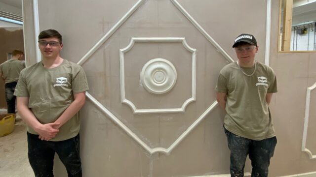 Two students stand in front of a wall that has recebtly been plastered.