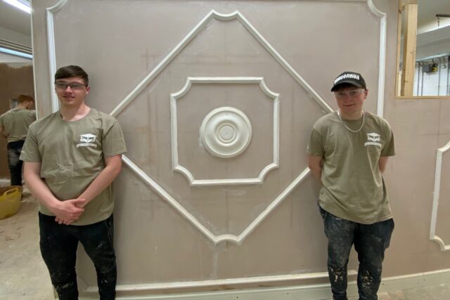 Two students stand in front of a wall that has recebtly been plastered.