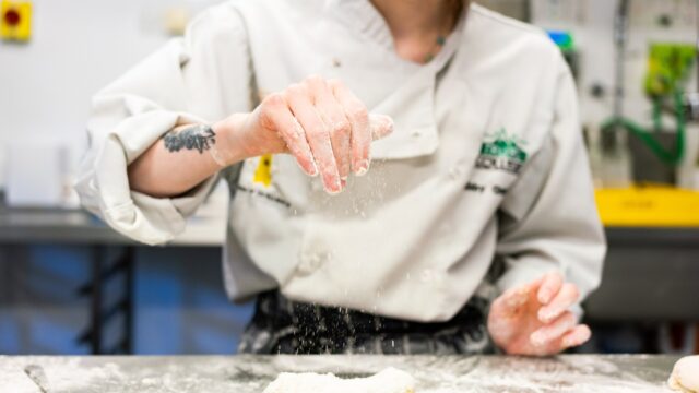 A close up of chef's hands sprinkling flour onto a surface.