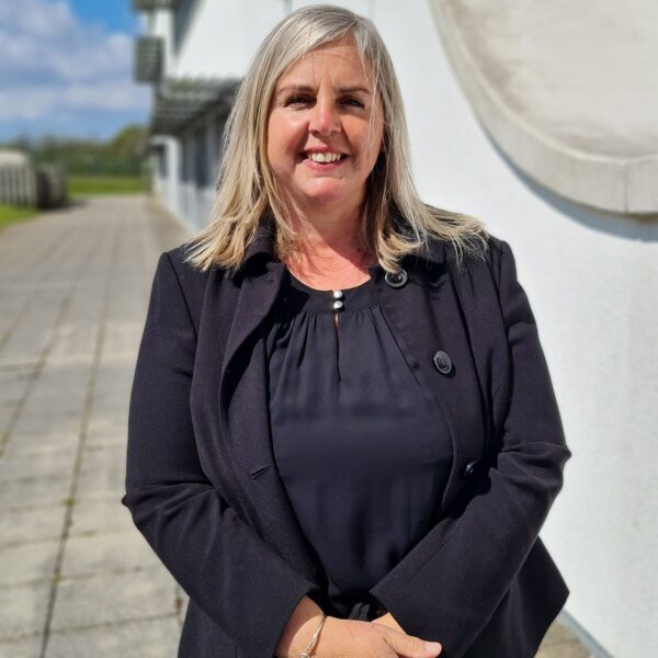 Nikki is stood outside in a dark suit on a sunny day.