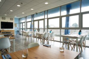 A photo of the inside of the Senara restaurant. There are wood tables and white chairs and large windows across the wall.