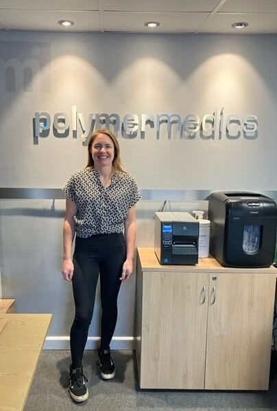 Sharon is stood next to a cabinet with the word polymermedics behind her.