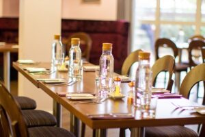 A photo of a long table with cutlery, glasses, water jugs and salt and pepper.
