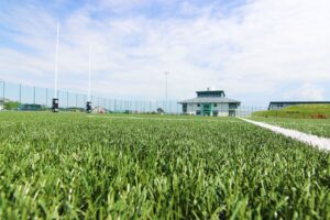 A close up of the grass on the astroturf with college buildings in the horizon.