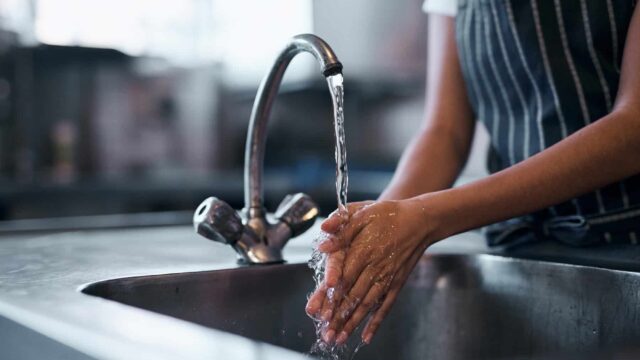 Close up of hands being washed in a kitchen sink.