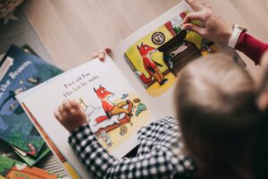 A child and an adult look at a picture book together. The page open shows a fox with the words 'Poor old fox has lost his socks'.